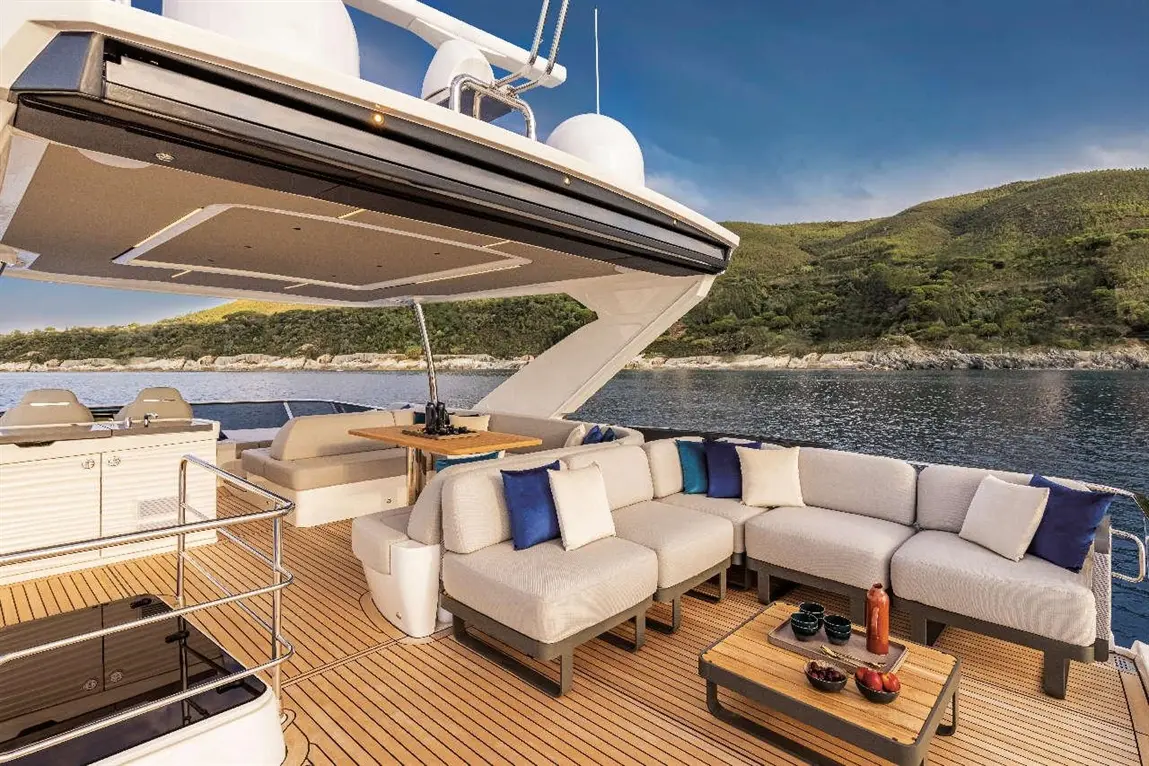 Luxurious yacht deck featuring a seating area with cushions, a wooden table, and a scenic coastal view in the background.